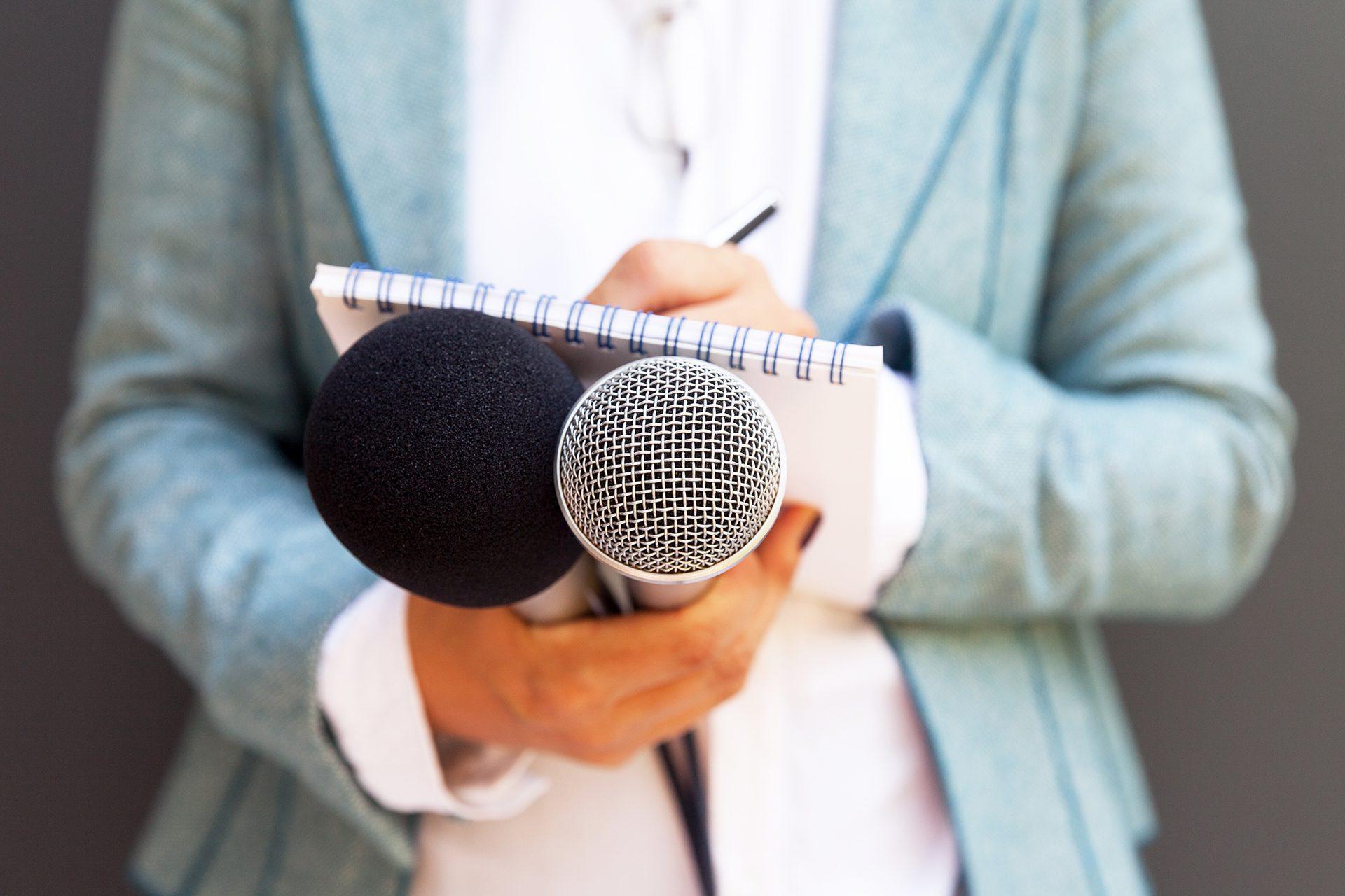 Female reporter at press conference, writing notes, holding microphone